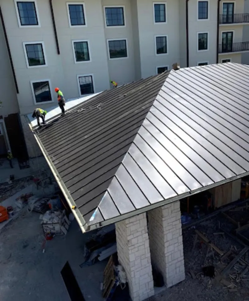 Crew installing standing seam metal roof panels on a commercial project in Old Westbury
